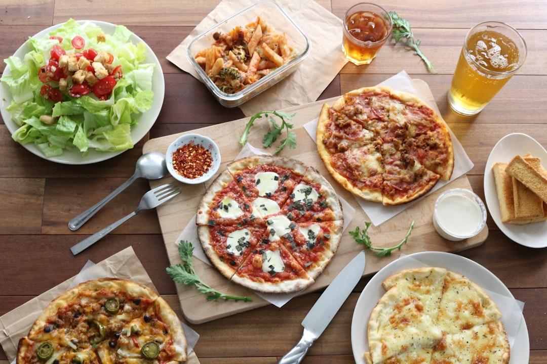Overhead view of fast food spread with pizzas, salad, fried appetizers, drinks, and bread on wooden table