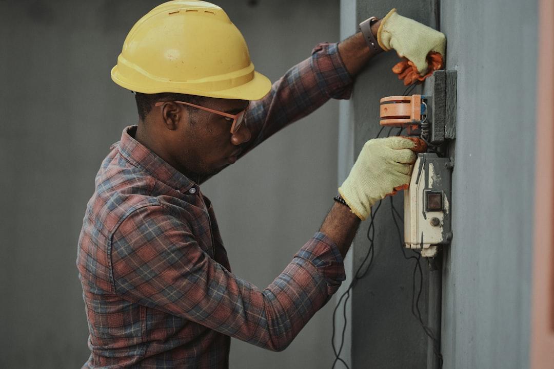 Professional handyman in yellow hard hat and work gloves installing electrical outlet on wall