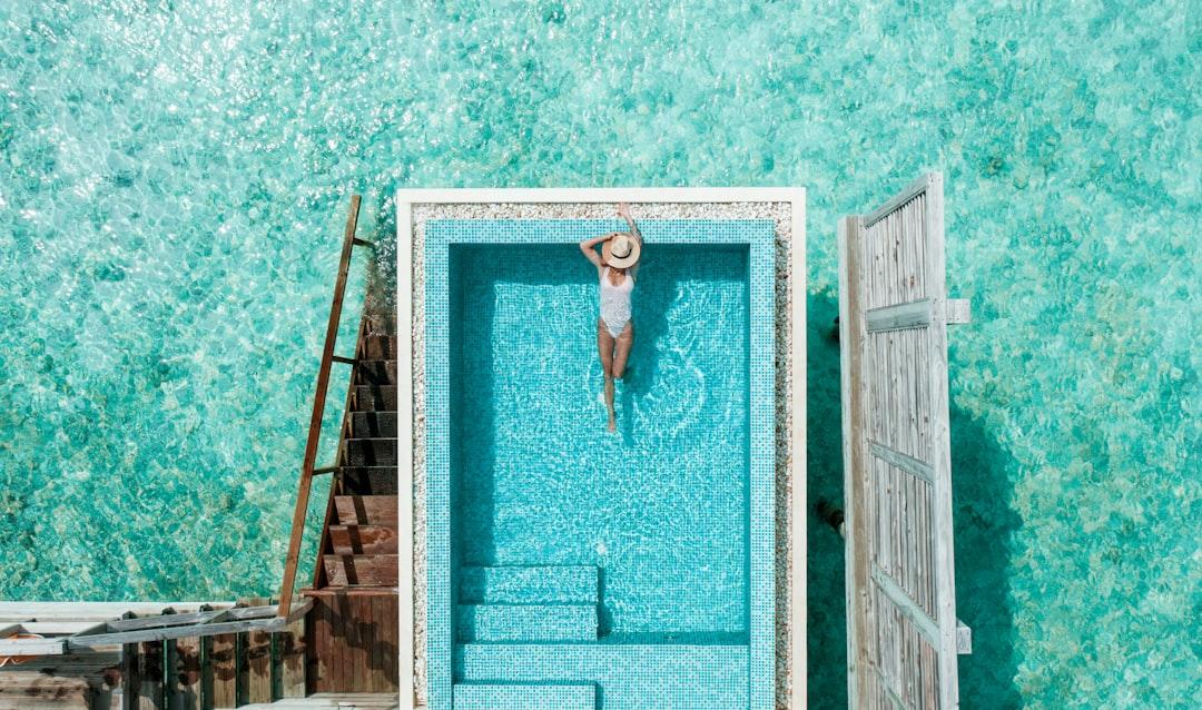 Aerial view of person relaxing in turquoise pool by wooden dock and white doors