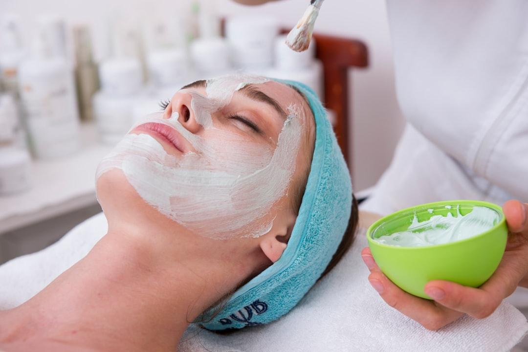 Esthetician applying white facial mask to client's face in spa treatment room