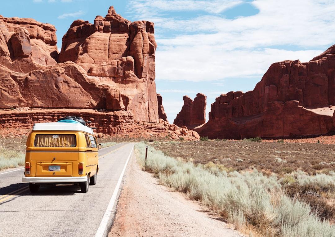 Vintage yellow camper van driving on desert road with red rock formations in background