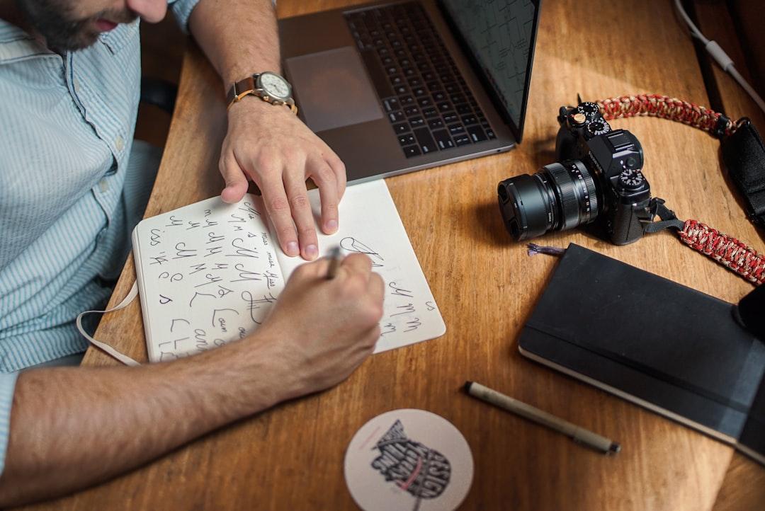 Designer sketching marketing strategy with camera, laptop, and notebook on wooden desk