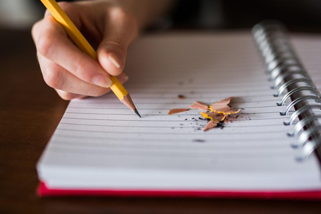 Hand holding sharpened pencil over spiral notebook with pencil shavings on lined paper