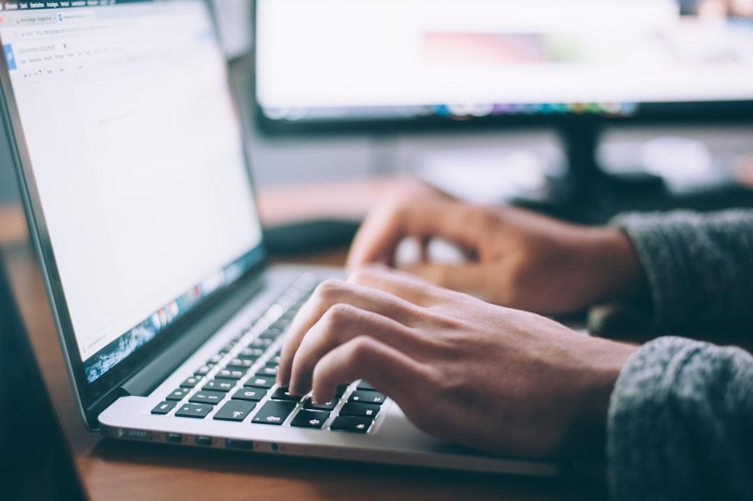 Person typing on laptop keyboard with multiple monitors displaying web design interface in background