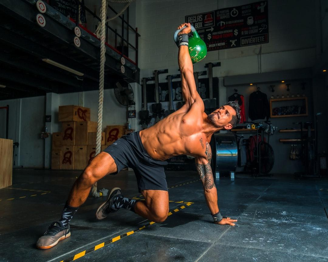 Muscular man performing kettlebell Turkish get-up exercise in a crossfit gym facility