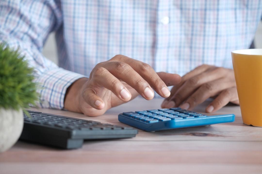 Person using blue calculator and keyboard at desk with coffee cup and plant