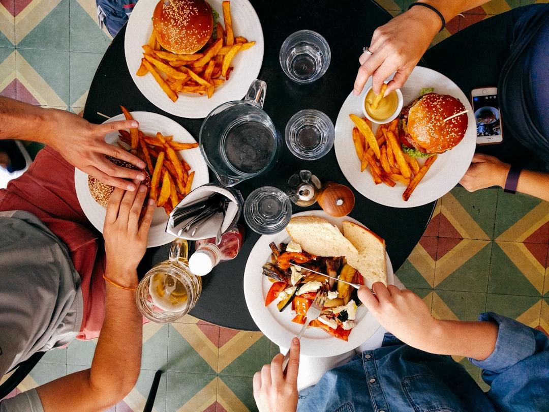 Overhead view of friends sharing burgers, fries, and drinks at a black table with colorful tile floor.